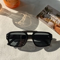 Close-up of double-bridge oversized square sunglasses on textured stone surface - Black