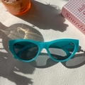 Detail of turquoise cat-eye sunglasses on a white table with summer lifestyle props - Blue