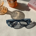 Cat eye sunglasses with blue-gray frames on a minimalist textured surface with lifestyle props - Transparent Blue