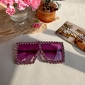 Oversized square sunglasses with purple rhinestones and gradient lenses on a desk - Purple