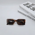 Detail view of tortoiseshell rectangle sunglasses with dark lenses on minimalist books - Tortoise Brown