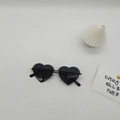 Détail de lunettes de soleil en forme de cœur avec pois blancs et verres foncés sur fond gris - Monture Noire Verres Gris