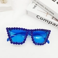 Dettaglio di occhiali da sole cat-eye blu con grandi strass su sfondo minimalista - Blu scuro