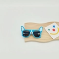 Blue dog-shaped children's sunglasses with white ears and cute nose details on a wooden surface - Sky Blue