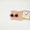 Detail of pink cartoon kids sunglasses with colorful parrot wings and crest on a wooden stand - Pink