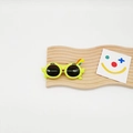 Detail of yellow parrot cartoon kids sunglasses with cute face on wavy wooden display - Green