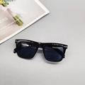 Flat lay of square black sunglasses with silver rivet accents on a grey surface - Black Frame Grey Lens