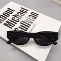 Detalle de gafas de sol cat-eye negras con remaches plateados sobre fondo de libro - Negro Brillante