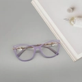 Dettaglio di occhiali cat-eye lavanda con stanghette dorate su sfondo di rivista minimale - Viola Gelatina