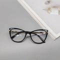 Dettaglio montatura cat-eye nera con eleganti aste in metallo dorato su una rivista - Nero Lucido