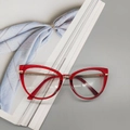 Detail einer roten Katzenaugen-TR90-Brille mit goldenen Metallbügeln auf Magazin-Hintergrund - Transparent Tee