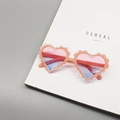 Close-up of pink glitter heart sunglasses for kids with gradient lenses on a magazine - Pink