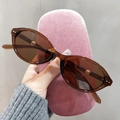 Close-up of translucent tawny cat eye sunglasses held with a pink velvet hard case - Transparent Dark Tea