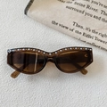 Detail einer braunen Cat-Eye-Sonnenbrille mit edlem Perlenbesatz und Metallnieten-Akzenten - Transparenter Dunkler Tee
