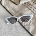 Dettaglio di occhiali da sole cat-eye bianchi con lenti grigie su sfondo di lino - Montatura bianca con lente grigia