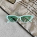 Dettaglio di occhiali da sole cat-eye verde menta su un tessuto con motivo retrò - Montatura Verde Menta Lenti Verdi