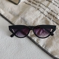 Close-up of black cat-eye sunglasses with dark purple lenses on white textured fabric - Black Frame Purple Gradient Lens