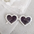 Detail view of white heart-shaped sunglasses with wavy scalloped frames on a textured base - Pixel White