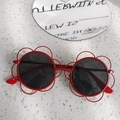 Dettaglio di occhiali da sole per bambini a forma di fiore rosso con lenti tonde scure - rosa rossa
