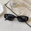 Modern black cat-eye sunglasses with dark lenses on a textured lifestyle background - Black Frame / Gray Lens