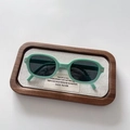 Detail view of foldable mint green kids sunglasses with oval frames on a wooden tray - Green