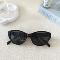 Close-up of retro black cat-eye sunglasses on a white tray with lifestyle decor items - Black Frame Grey Lens