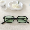 Lunettes de soleil rétro à monture noire et verres vert clair sur une table blanche chic - Monture Noire Verres Verts