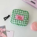 Detail of green checkered quilted pouch with pink label and black zipper pull on white desk - Green
