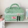 Detail of green and white plaid quilted cosmetic bag with pink zippers on a shelf - Green