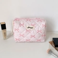 Pink quilted makeup bag with bow print and brand tag displayed with cosmetics - Pink Bowknot