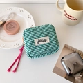 Close-up of green checkered quilted pouch with orange zipper and pink cord details - Green