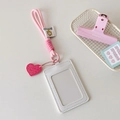 Vertical white ID card holder with pink braided lanyard and heart pendant on white desk - White