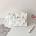 Detail of white quilted cosmetic bag featuring butterfly embossing and ribbon zipper pull - White