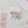 Close-up of 6pc 25mm cartoon tinplate badges with apple and clover icons on pink card - House & Clover (6Pcs Set)