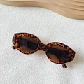 Retro-Cat-Eye-Sonnenbrille mit Schildpatt-Muster und dunklen Gläsern auf hellem Sockel - Leopardenmuster