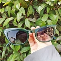 Retro dark green cat-eye sunglasses with dark lenses held against a lush green background - 56-15-139 C2 / Dark Green