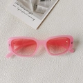 Gros plan de lunettes de soleil rectangulaires roses sur une surface texturée blanche - Monture Rose Gelée Verre Rose