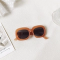 Detalle de gafas de sol ovaladas con montura naranja gruesa y lentes oscuras sobre encaje - Color Té con Leche