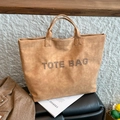 Tan PU leather tote bag with rivet-studded lettering in a stylish casual setting - Brown