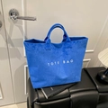 Blue suede tote bag with white text print on a black stool for a minimalist aesthetic - Blue