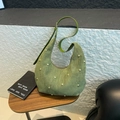 Detail der grünen Wildleder-Tasche mit goldenen Nieten auf einem Holztisch - Grasgrün