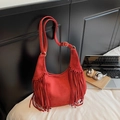 Red suede hobo bag with bohemian fringe detail and adjustable strap on a bed - Red