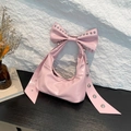 Rosa Handtasche in Schleifenform mit Glanzeffekt und Silbernieten auf Holztisch - Rosa