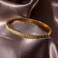 Luxe gold stainless steel bangle with diamond rhombus pattern on purple silk backdrop - Gold