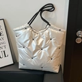 Metallische Puffer-Tasche mit Sternenstickerei und Kordelgriffen auf Ledersofa - Weiß