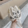 Detail der weißen Eimertasche aus Kieselleder mit THE BUCKET Druck und Gold-Hardware - Weiß
