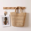 Bolso tote de rafia calado en color beige para playa colgado de un gancho de madera - Color Original