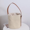 Minimalistische Stroh-Eimertasche in Cremeweiß mit braunem Lederriemen auf weißem Tisch - Beige
