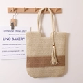 Beige and dark coffee two-tone woven straw tote bag with tassel hanging on a hook - Beige