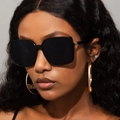 Detail of black oversized square sunglasses paired with gold sun hoop earrings on a model - Bright Black / Gray